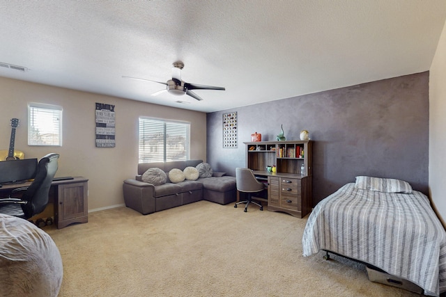 bedroom with a ceiling fan, visible vents, light carpet, and a textured ceiling