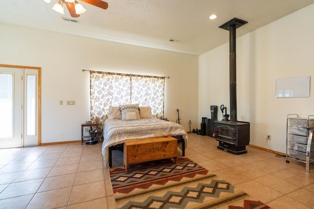 bedroom with a wood stove, light tile patterned floors, baseboards, and visible vents