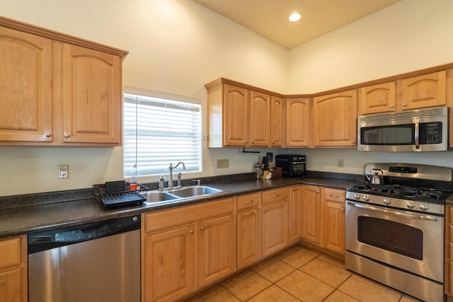 kitchen with appliances with stainless steel finishes, dark countertops, a sink, and light tile patterned floors