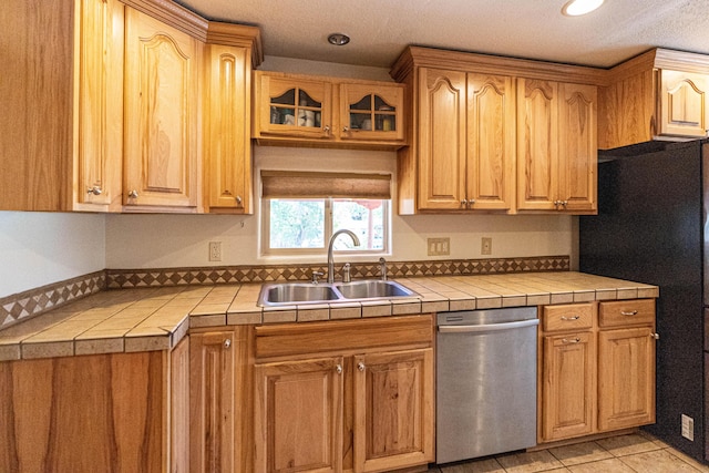 kitchen with tile countertops, a sink, freestanding refrigerator, dishwasher, and glass insert cabinets