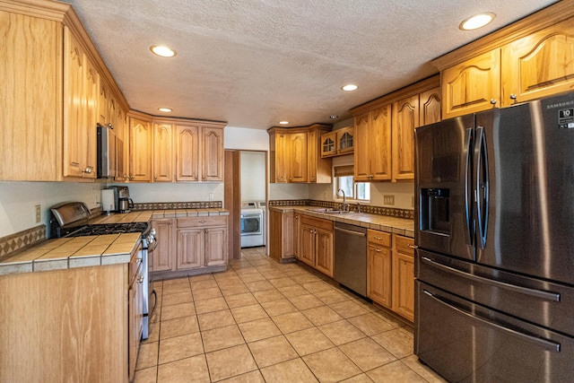 kitchen with tile countertops, recessed lighting, stainless steel appliances, a sink, and washer / clothes dryer