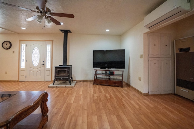 living area with light wood-style flooring, a wall mounted AC, a ceiling fan, a wood stove, and a textured ceiling