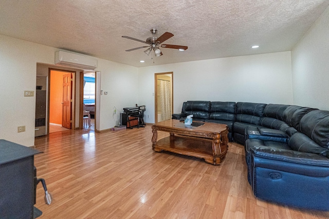 living room featuring a textured ceiling, an AC wall unit, light wood-type flooring, and a ceiling fan