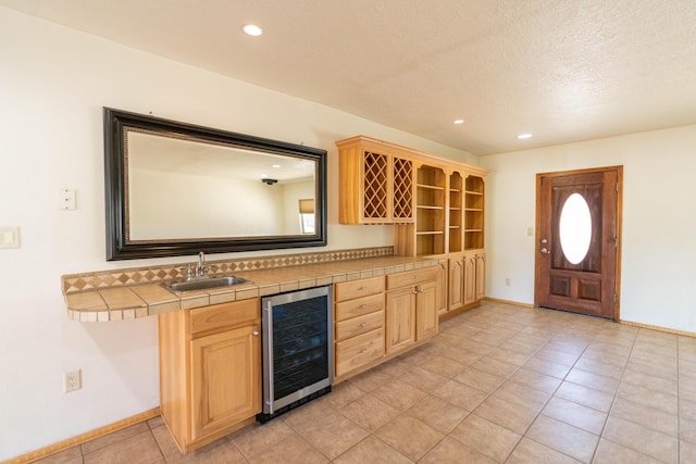 kitchen with beverage cooler, tile countertops, a textured ceiling, light brown cabinets, and a sink