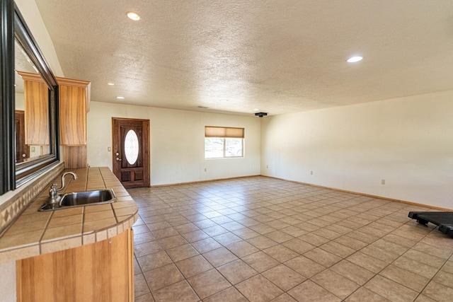 interior space with a sink, a textured ceiling, baseboards, and light tile patterned floors