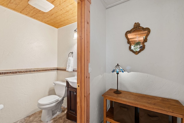 bathroom featuring toilet, a textured wall, and vanity