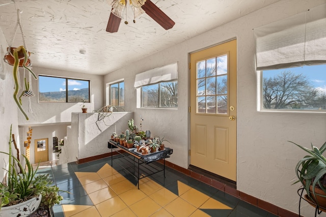 tiled entryway featuring a textured wall, a ceiling fan, and baseboards