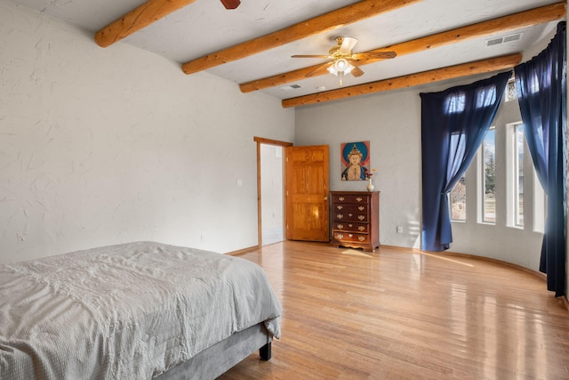 bedroom featuring baseboards, visible vents, a textured wall, wood finished floors, and beam ceiling