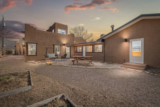 rear view of house with stucco siding, a garden, and a patio