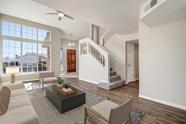 living area featuring stairs, visible vents, wood finished floors, baseboards, and ceiling fan with notable chandelier