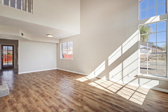 unfurnished living room featuring wood-type flooring, visible vents, a towering ceiling, and baseboards