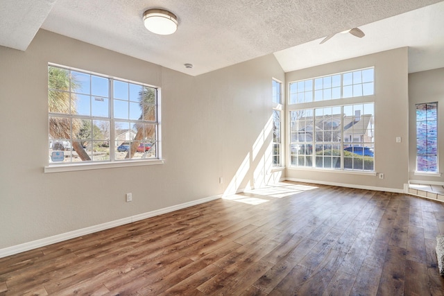 unfurnished room with a textured ceiling, baseboards, and wood finished floors