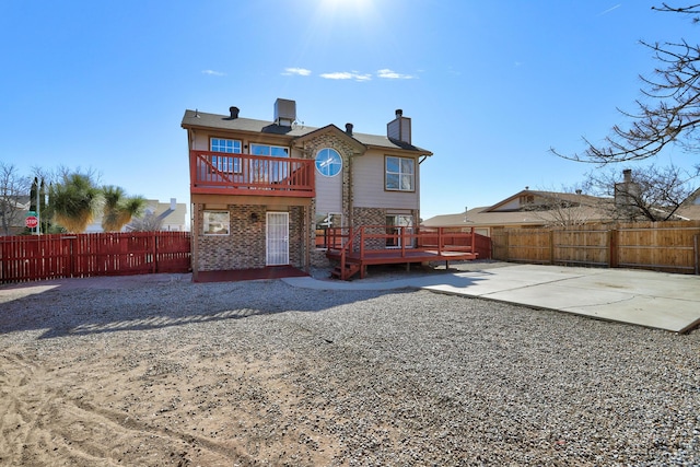 rear view of property with a fenced backyard, a patio, a wooden deck, and brick siding