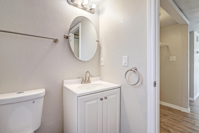 bathroom with a textured wall, toilet, vanity, wood finished floors, and baseboards