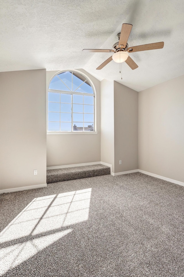 carpeted empty room with a textured ceiling, a ceiling fan, and baseboards