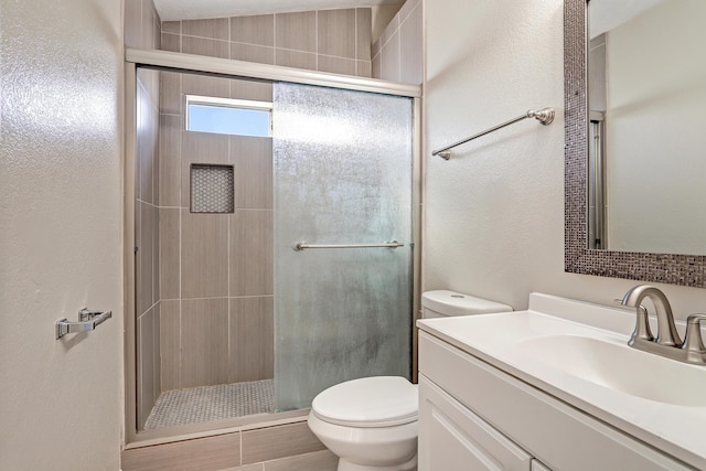 bathroom with a textured wall, a shower stall, toilet, and vanity