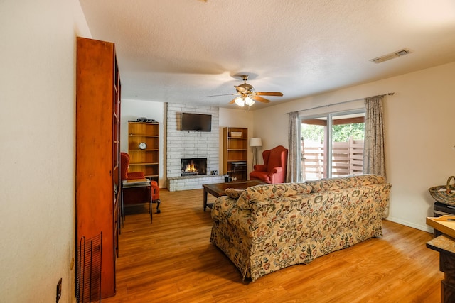 living room featuring light wood-type flooring, a brick fireplace, visible vents, and a textured ceiling