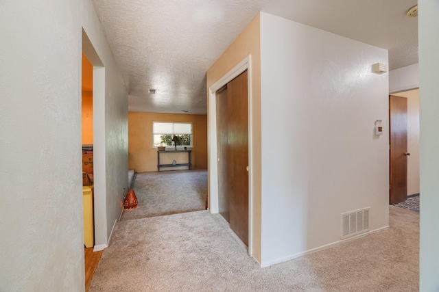 hallway featuring carpet, visible vents, and a textured ceiling