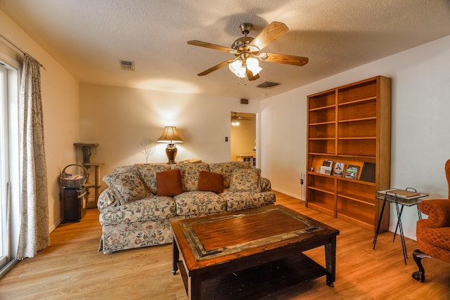 living area featuring a textured ceiling, light wood finished floors, visible vents, and a ceiling fan