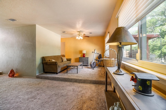 living room with a textured ceiling, carpet floors, visible vents, and a ceiling fan