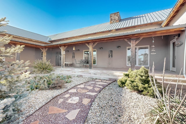 rear view of property with a patio area, a chimney, metal roof, and stucco siding