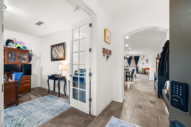 interior space featuring baseboards, visible vents, arched walkways, wood finished floors, and a textured ceiling