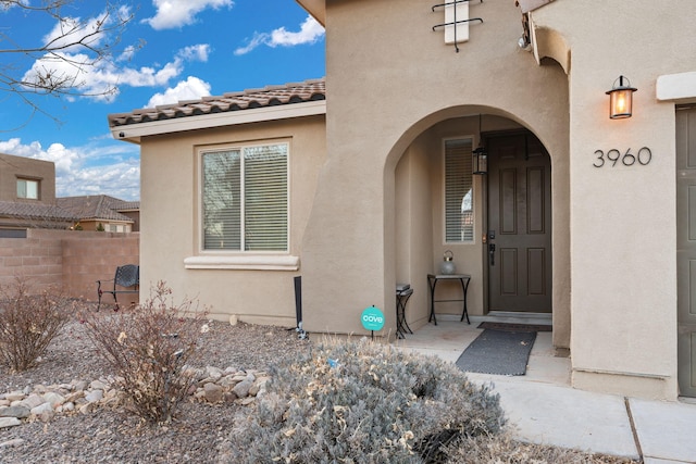 property entrance with a tile roof, fence, and stucco siding