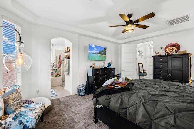 carpeted bedroom featuring visible vents, arched walkways, connected bathroom, ceiling fan, and a tray ceiling