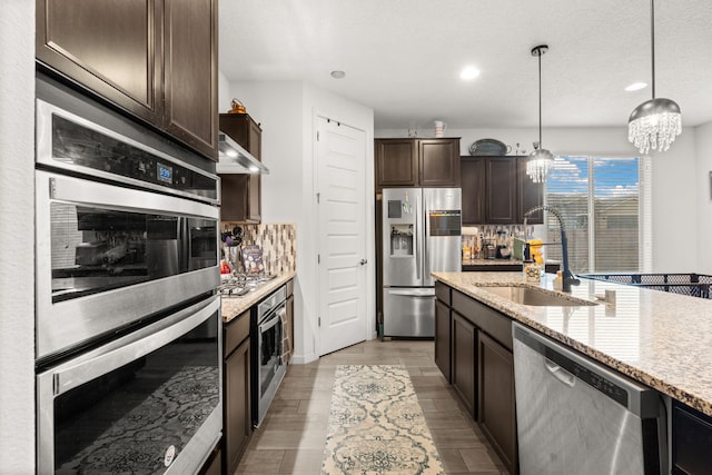 kitchen with light stone counters, pendant lighting, stainless steel appliances, a sink, and dark brown cabinetry