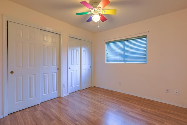 unfurnished bedroom with a ceiling fan, baseboards, multiple closets, and wood finished floors