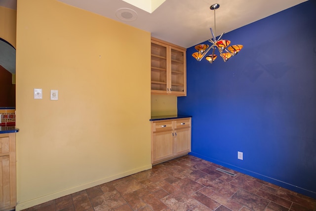 unfurnished dining area featuring a notable chandelier, stone finish flooring, visible vents, and baseboards