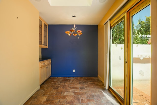 unfurnished dining area featuring stone finish flooring, baseboards, and a notable chandelier