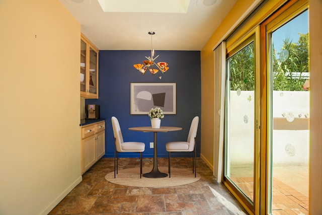 dining space with a notable chandelier, stone finish floor, and baseboards