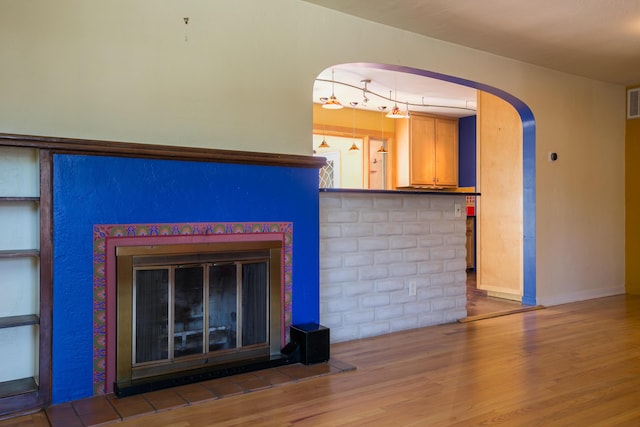 unfurnished living room featuring arched walkways, a fireplace, wood finished floors, visible vents, and baseboards