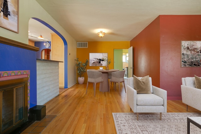 dining area featuring a brick fireplace, visible vents, arched walkways, and wood finished floors