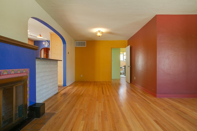 unfurnished living room with arched walkways, a fireplace, wood finished floors, visible vents, and baseboards