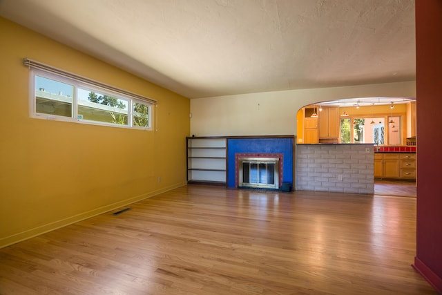 unfurnished living room featuring a glass covered fireplace, wood finished floors, and a wealth of natural light