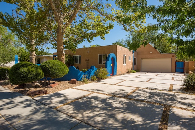 pueblo-style home featuring a garage, concrete driveway, and stucco siding