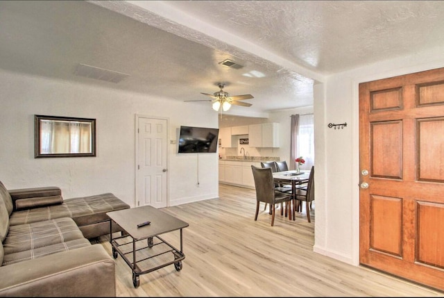 living area with light wood-type flooring, ceiling fan, visible vents, and a textured ceiling