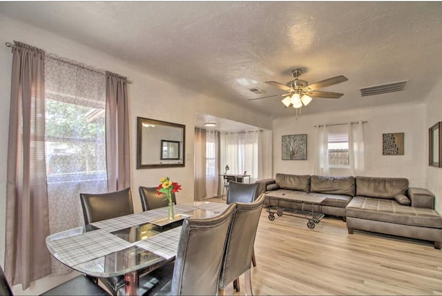 dining room featuring light wood-style flooring, visible vents, ceiling fan, and a textured ceiling