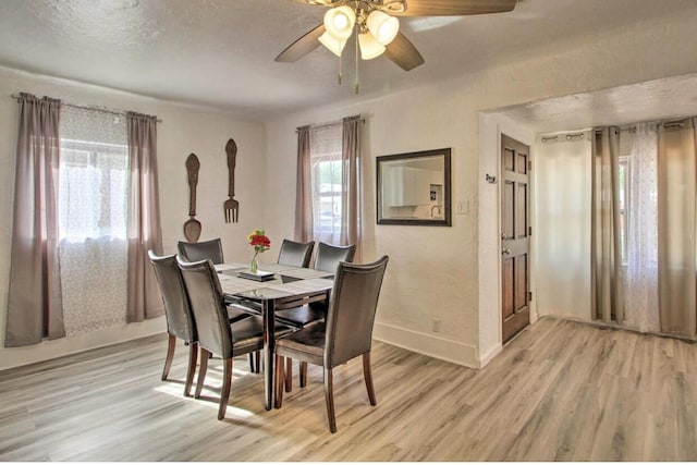 dining room featuring light wood finished floors, ceiling fan, baseboards, and a textured ceiling