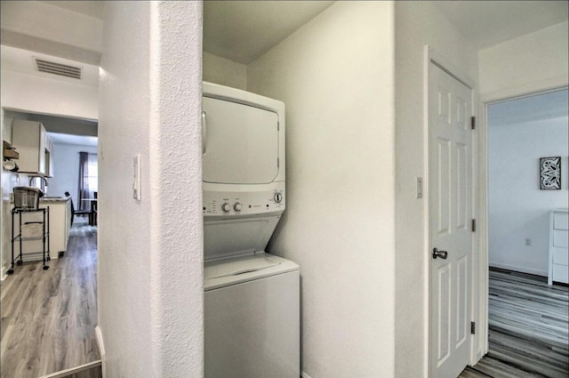 clothes washing area featuring laundry area, stacked washer and clothes dryer, visible vents, and wood finished floors