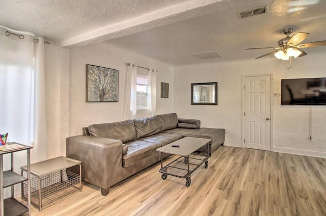 living room with light wood-type flooring, visible vents, ceiling fan, and a textured ceiling