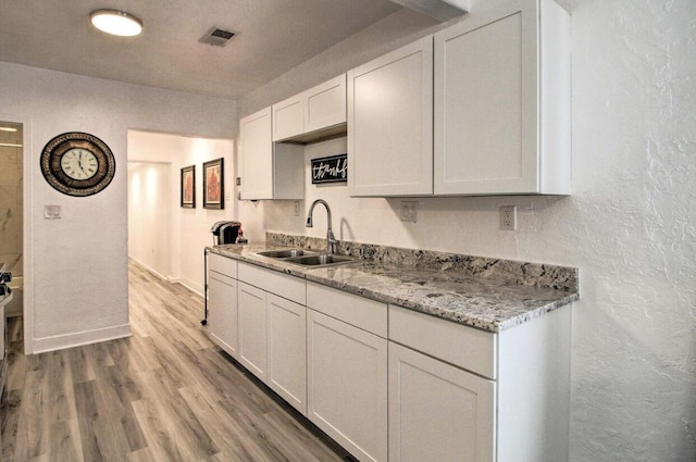 kitchen with a textured wall, a sink, white cabinets, light wood-style floors, and light stone countertops