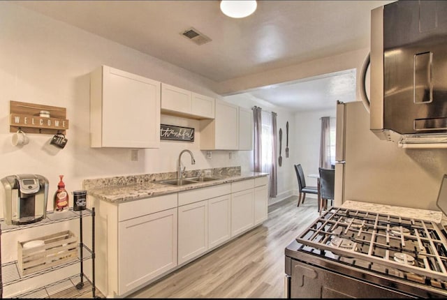 kitchen featuring light wood-style flooring, stainless steel appliances, a sink, visible vents, and white cabinets