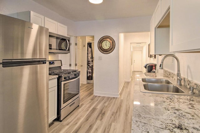 kitchen with light wood finished floors, white cabinets, light stone counters, stainless steel appliances, and a sink