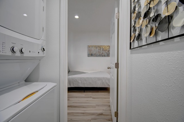 washroom featuring stacked washer / dryer, laundry area, a textured wall, and wood finished floors