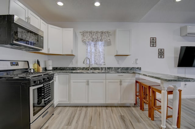 kitchen with stainless steel appliances, dark stone counters, a wall unit AC, and a sink