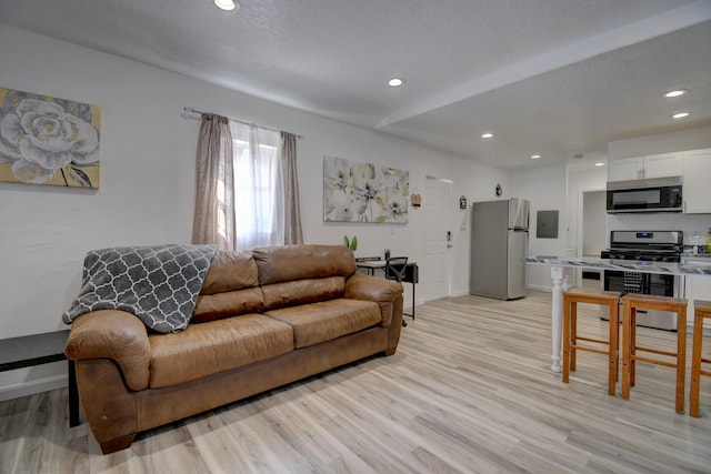 living room featuring a textured ceiling, light wood-type flooring, baseboards, and recessed lighting