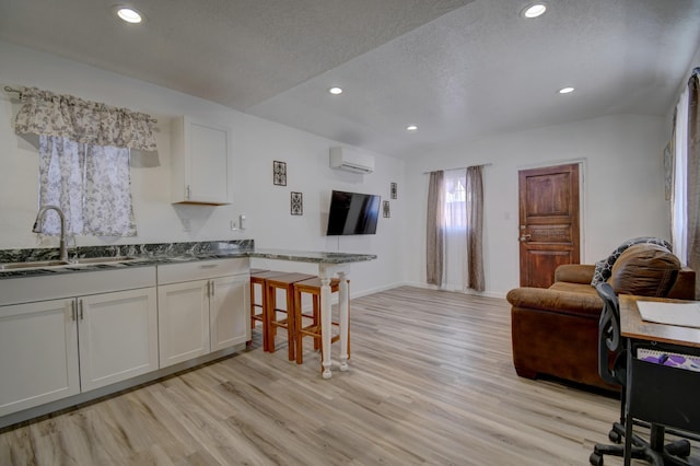 kitchen with light wood finished floors, white cabinets, a breakfast bar area, a textured ceiling, and a sink